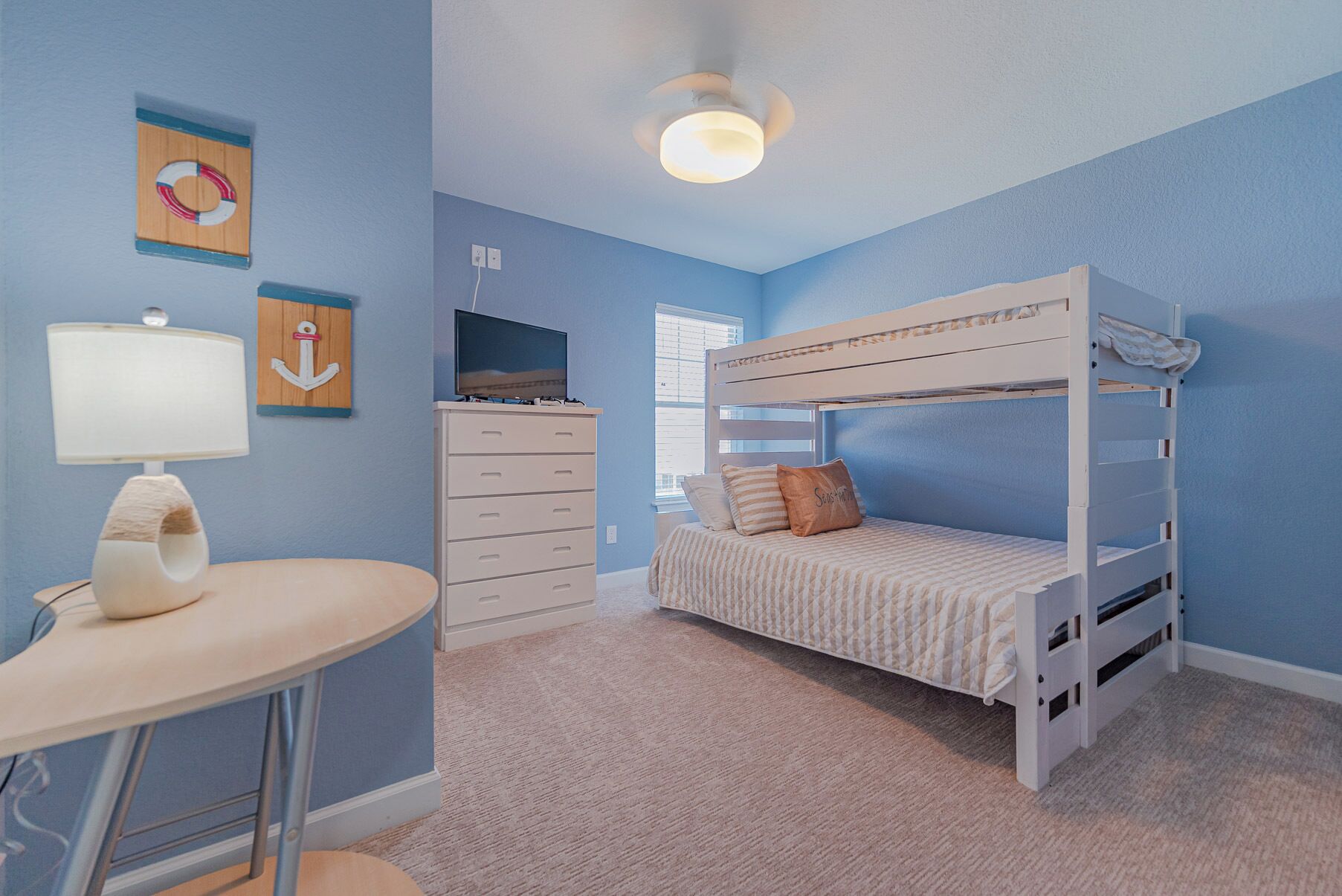 A child's bedroom with a bunk bed, a desk with a lamp, a dresser, and wall decorations.