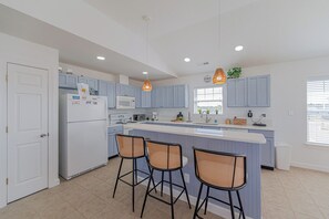 A modern kitchen with a central island, bar stools, and pendant lighting. - JL #313 Sea Bass - Hot Tub - Game Room - Close to Beach (Kill Devil Hills)