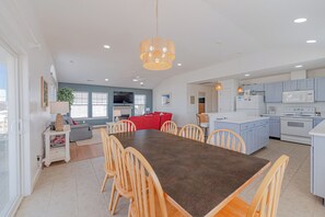 Une cuisine moderne avec un îlot central, un coin repas avec des chaises et un salon avec un canapé et une télévision.