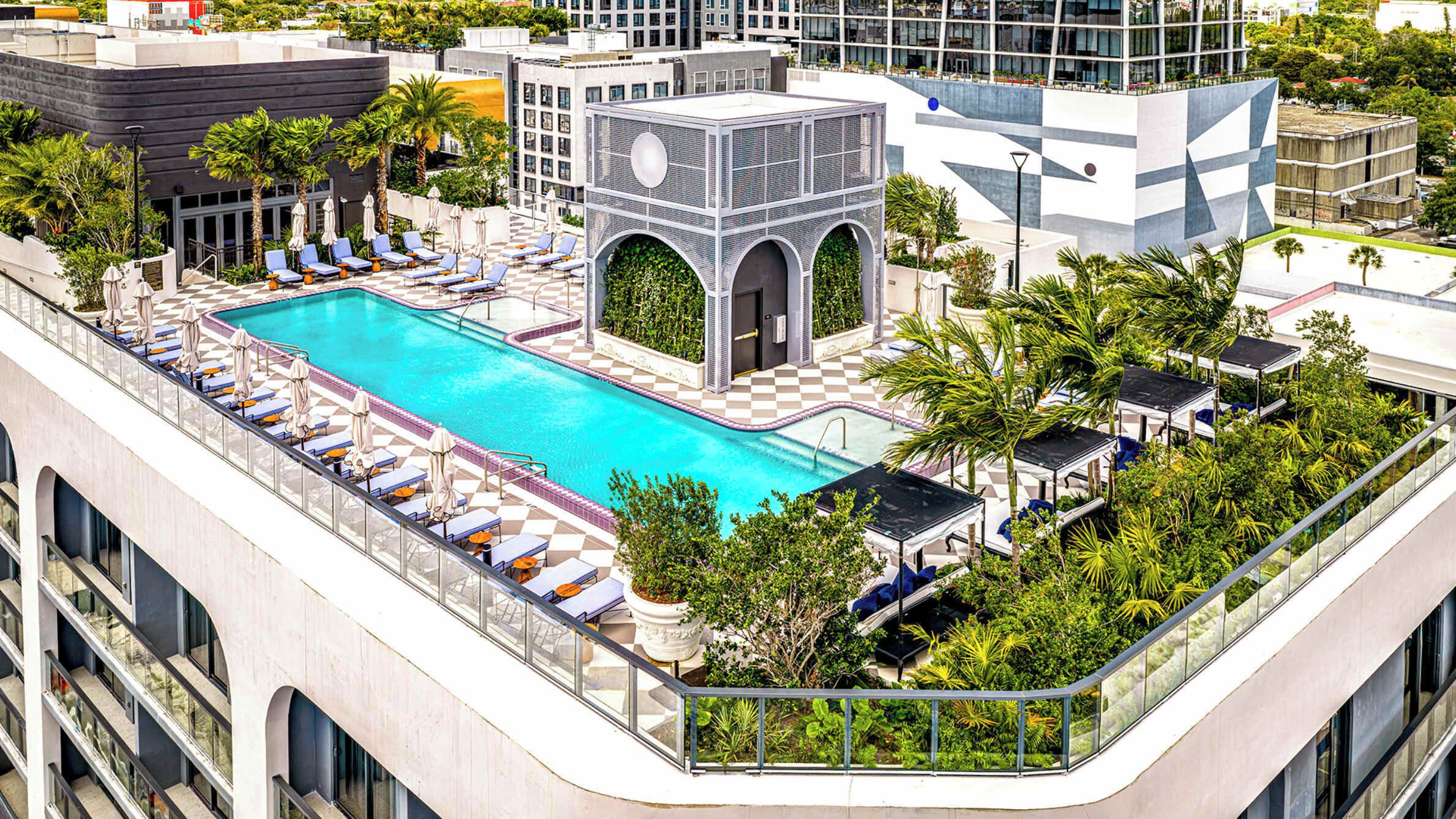 A rooftop swimming pool with lounge chairs and umbrellas, surrounded by greenery and modern architecture.