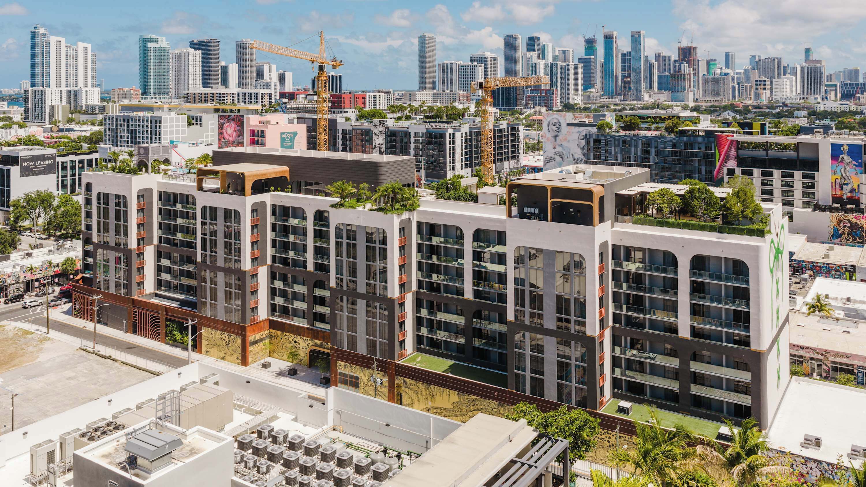 A modern high-rise building with multiple balconies and large windows, surrounded by other high-rise buildings and construction cranes.