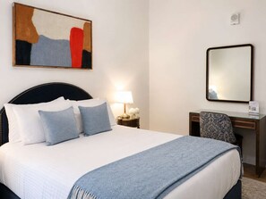 Una habitación de hotel con cama, mesita de noche, lámpara, silla y un cuadro en la pared.