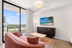 Ein modernes Wohnzimmer mit großem Fenster, einer Couch, einem Tisch, einem Schrank und einem Bild von einer Strandlandschaft.