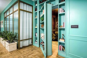 Ein raum in tealblau mit einem großen Fenster, einem Bücherregal und einem Schild mit der Aufschrift 'SPEAKEASY'.