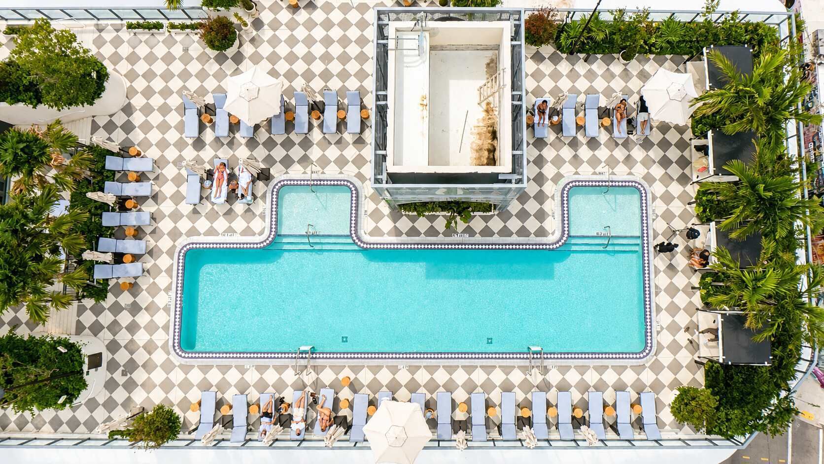 Une piscine sur le toit, dont le sol présente un motif à carreaux, entourée de chaises longues et de parasols.
