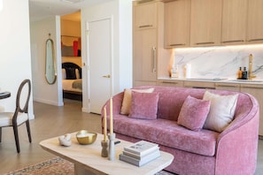 Una sala de estar moderna con un sofá rosa, una mesa de centro con adornos y vistas al dormitorio contiguo.