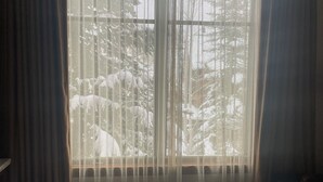 Een hotelkamer met een groot bed, dunne gordijnen en uitzicht op bomen.