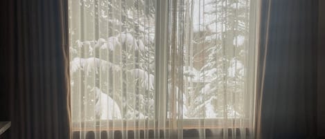 A hotel room with a large bed, sheer curtains, and a view of trees outside.