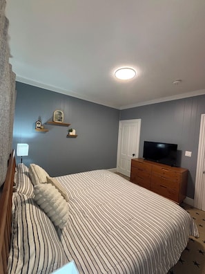 A bedroom with a bed, dresser, television, and wall-mounted shelves. - SAGE Boutique Retreat • Sleeps 6 (Burrillville)