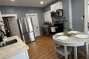A modern kitchen with stainless steel appliances, a dining area with a round table and chairs, and light grey cabinetry. - SAGE Boutique Retreat • Sleeps 6 (Burrillville)