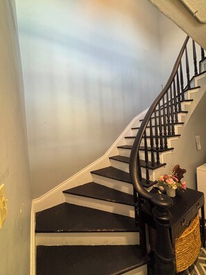A spiral staircase with black steps and a black handrail, leading to a landing with a small table holding a vase of flowers.