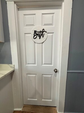 Eine weiße Tür mit einem runden Schild, auf dem 'Bath' steht.