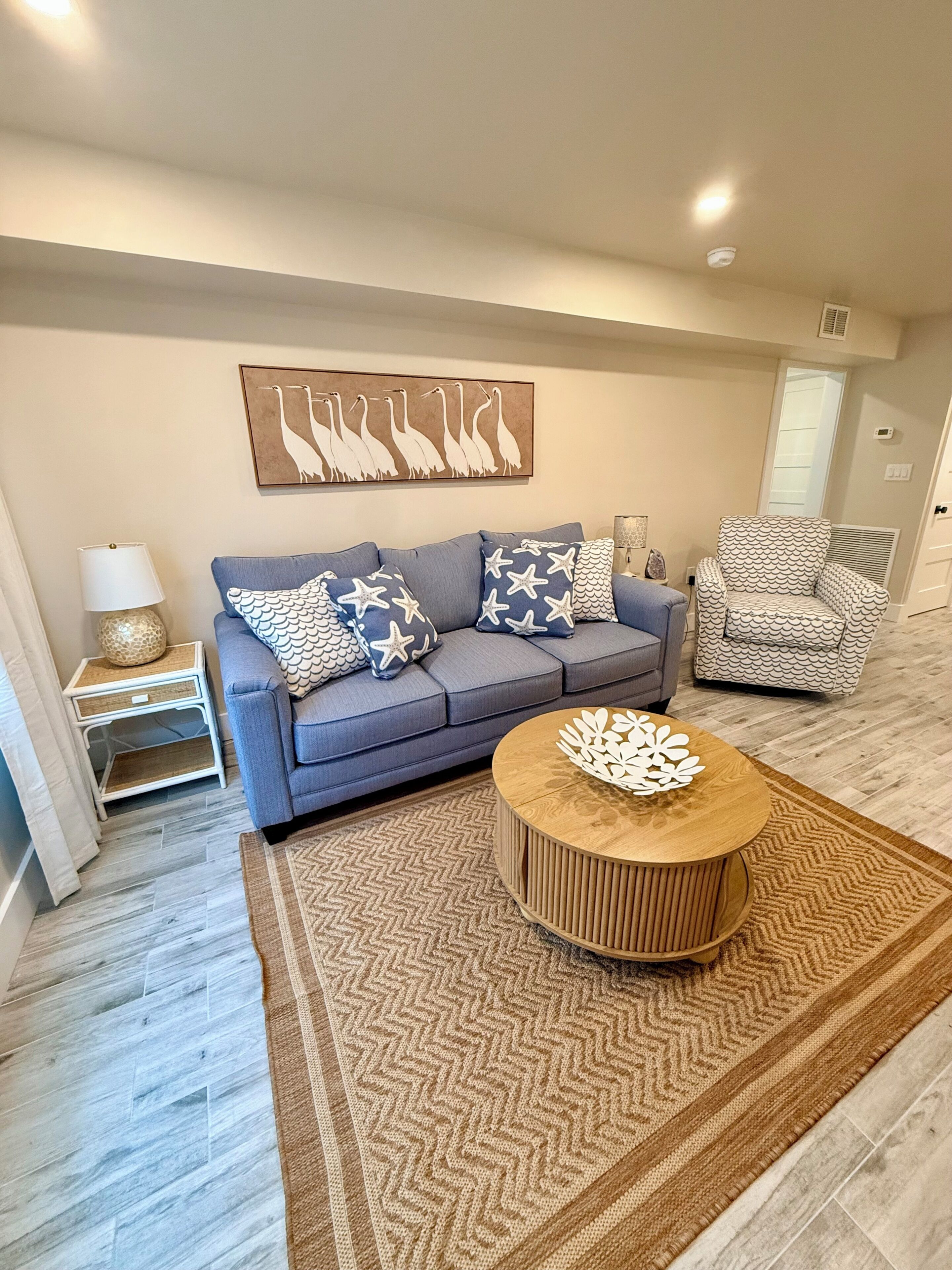 A living room with a grey sofa, patterned cushions, a round coffee table, and a wall-mounted artwork.