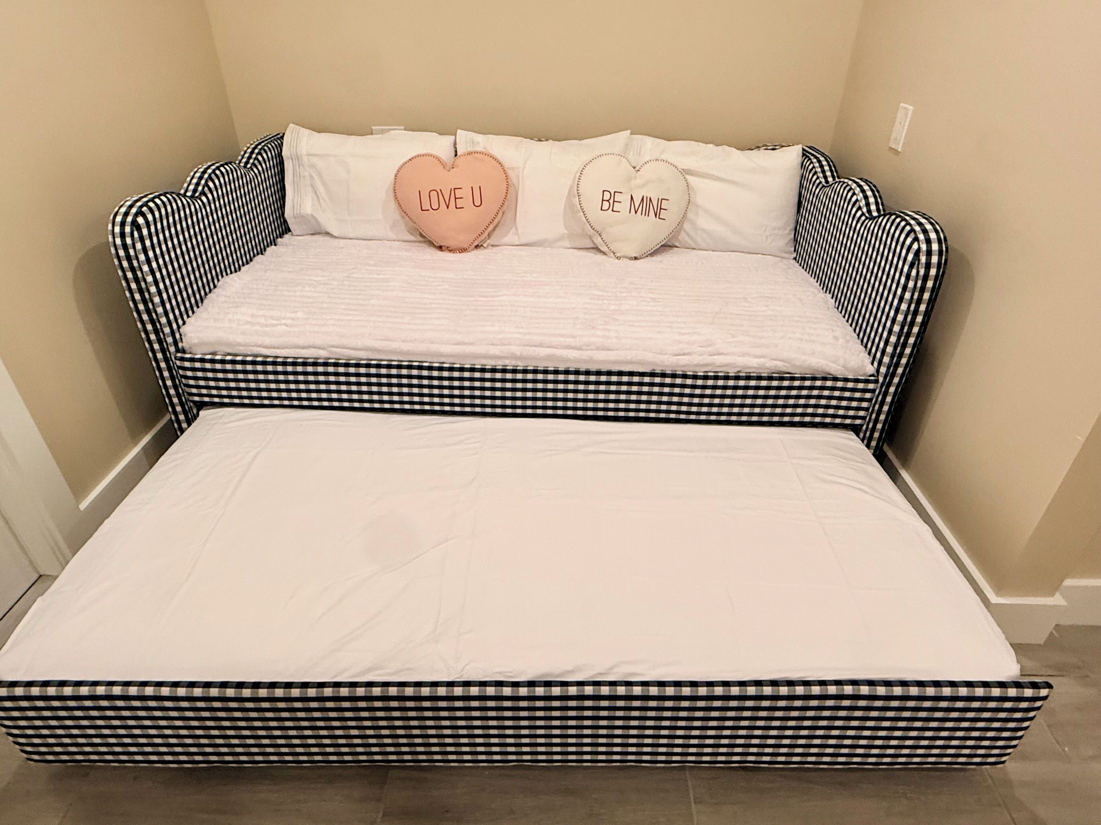 Ein Bett mit einem karierten Kopfteil und zwei herzenförmigen Kissen mit Aufschriften.