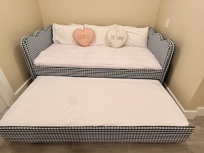 Een bed met een geruit hoofdbord en twee hartvormige kussens met teksten.