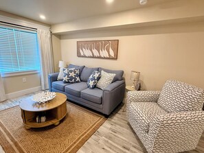 A living room with a grey sofa, patterned cushions, a round wooden coffee table, and a patterned armchair. - The Elli -indoor ping pong-3 bedrooms 2 bathrooms & outdoor shower (Bradenton)