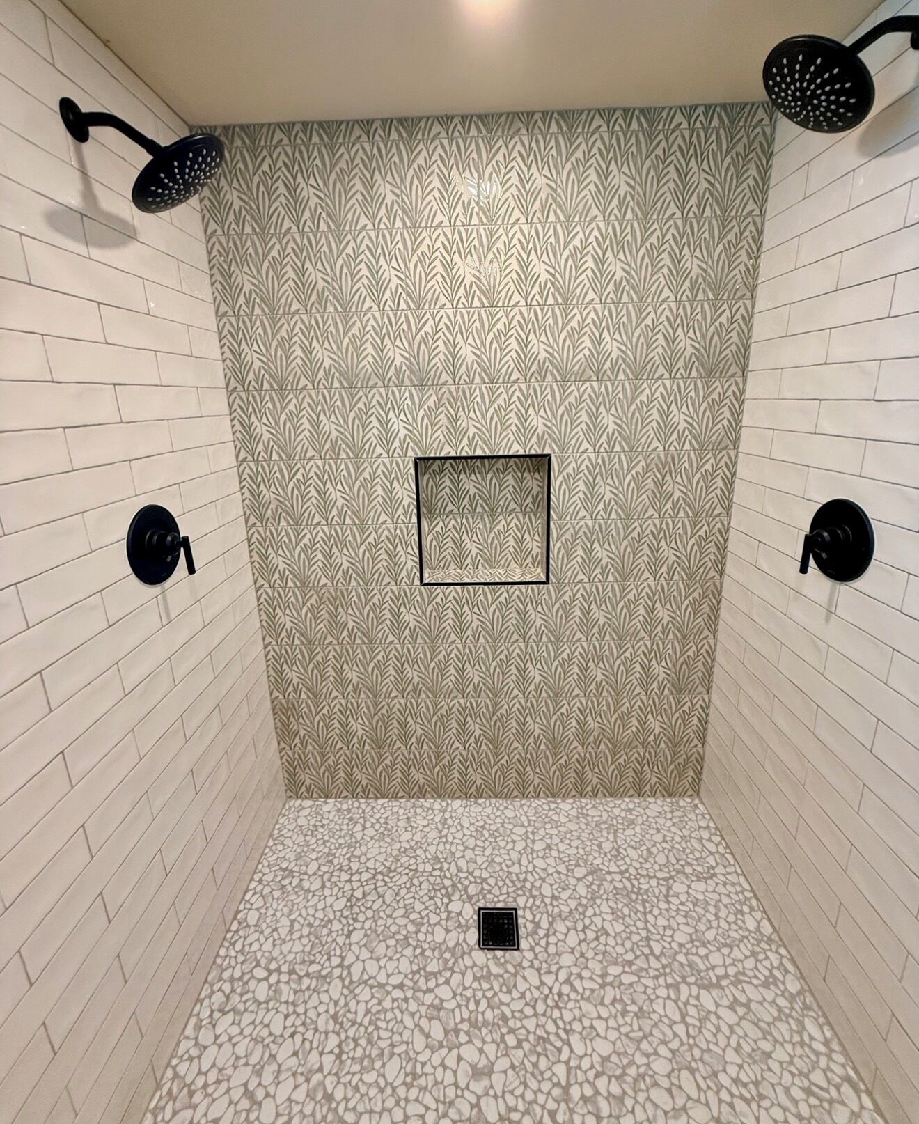 Un área de ducha con un revestimiento de pared estampado, una pequeña ventana cuadrada y un piso con textura de guijarros.