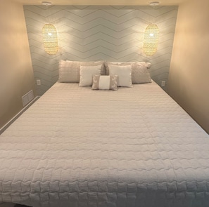 A bed with a textured white cover, flanked by two wall-mounted light fixtures and a chevron-patterned wall. - The Elli -indoor ping pong-3 bedrooms 2 bathrooms & outdoor shower (Bradenton)