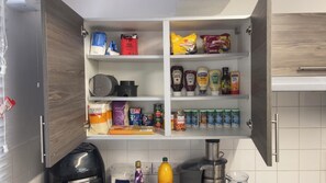 A kitchen with open cabinets displaying various food items and condiments. - Luxury 2-Bed London Flat | Free Parking, PS5 & Sleeps 6 (London)
