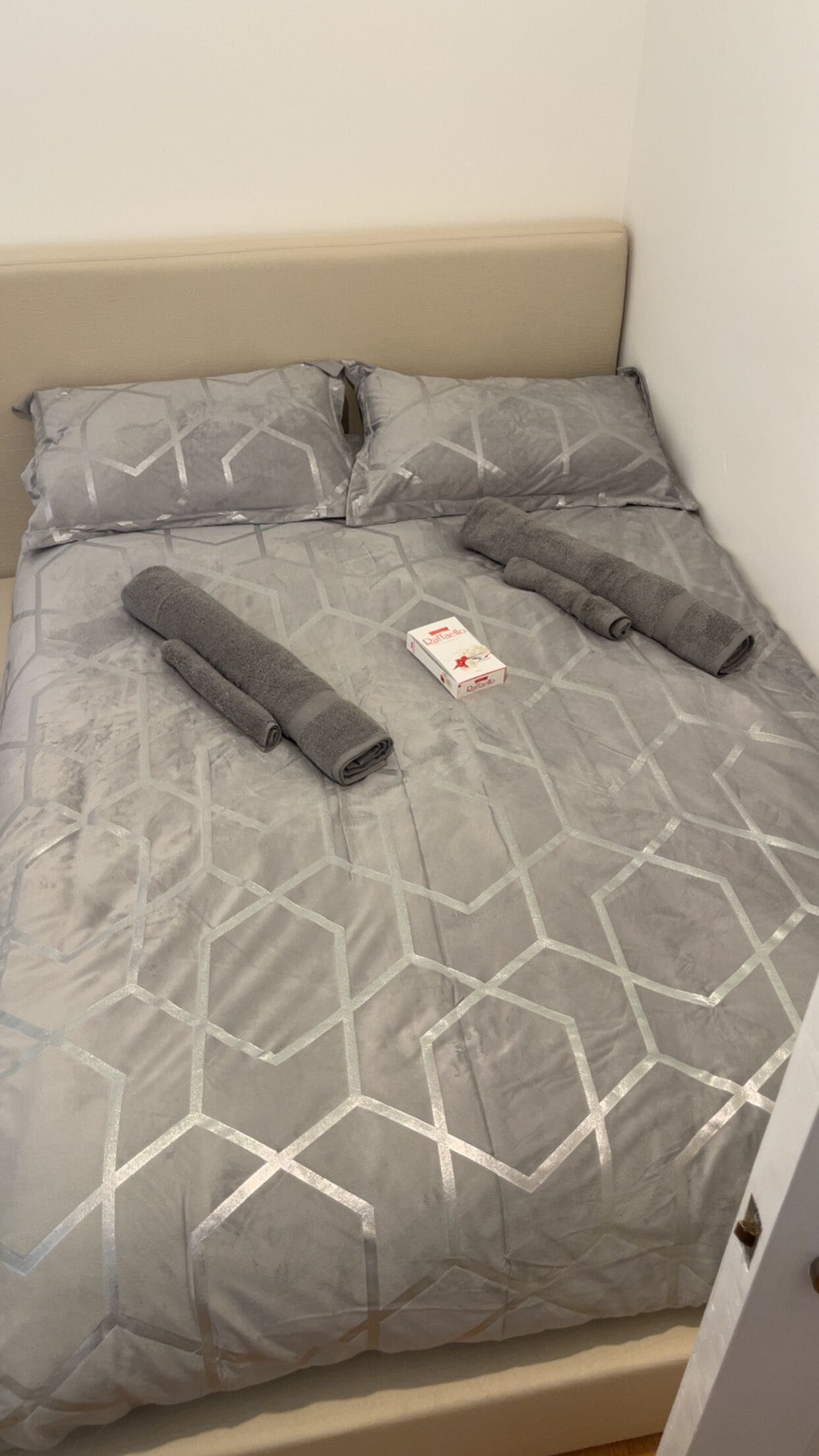 Ein Bett mit einem geometrisch gemusterten Überwurf, zwei aufgerollte Handtücher und einer Taschentuchbox.