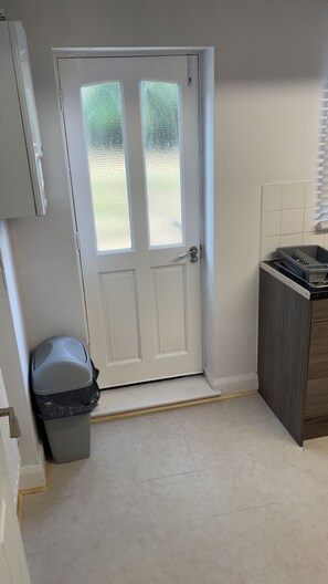 A kitchen with a white door, a trash bin, and a dishwasher. - Luxury 2-Bed London Flat | Free Parking, PS5 & Sleeps 6 (London)