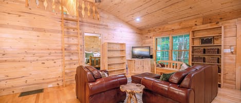 A wooden interior with a ceiling fan, a television, leather sofas, and a wooden ladder.