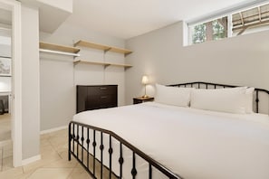 A bedroom with a bed, nightstand, lamp, and built-in shelving. - Bay Park Vacation House (San Diego)