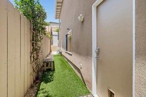 Ein schmaler Garten mit Holzlattenzaun, einer kleinen Bank und einer Tür auf der rechten Seite.