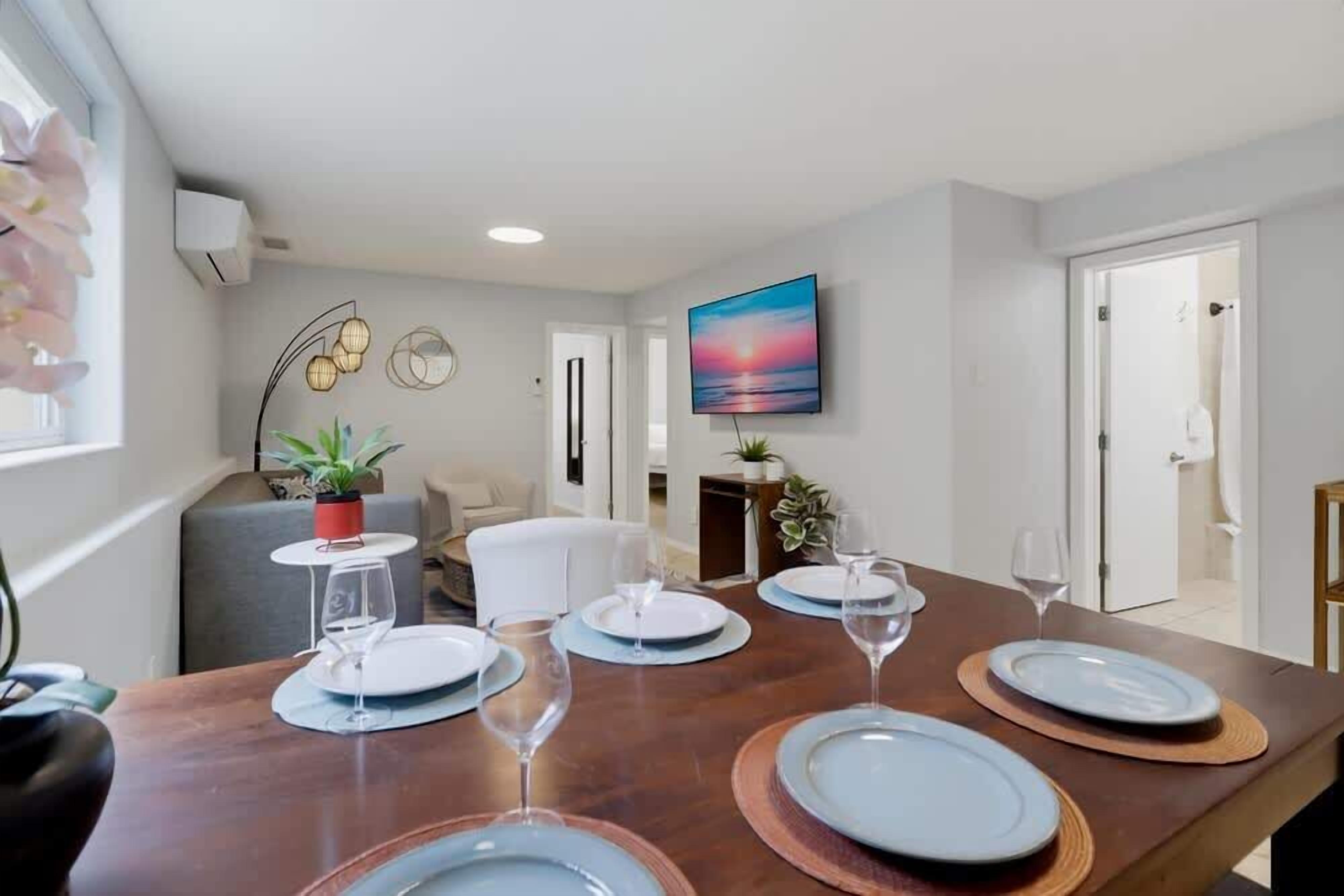 A dining area with a table set for four, a television mounted on the wall, and a view of the adjacent living room.