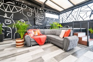 A modern living area with a sectional sofa, a red throw blanket, and decorative pillows. There are potted plants and a black wall with white abstract art. - Prado Centro #2 Luxury Suite - Jacuzzi & Balcony   (Medellín)