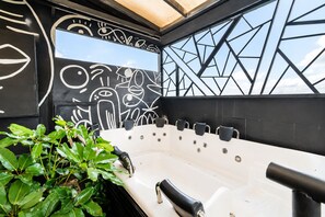 Un bain à remous extérieur moderne, doté de plusieurs jets, entouré de verdure et agrémenté d’un mur au design géométrique.