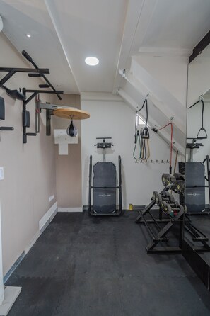 Une salle de sport équipée de divers appareils d’exercice, notamment un sac de frappe, des supports pour poids et un miroir.
