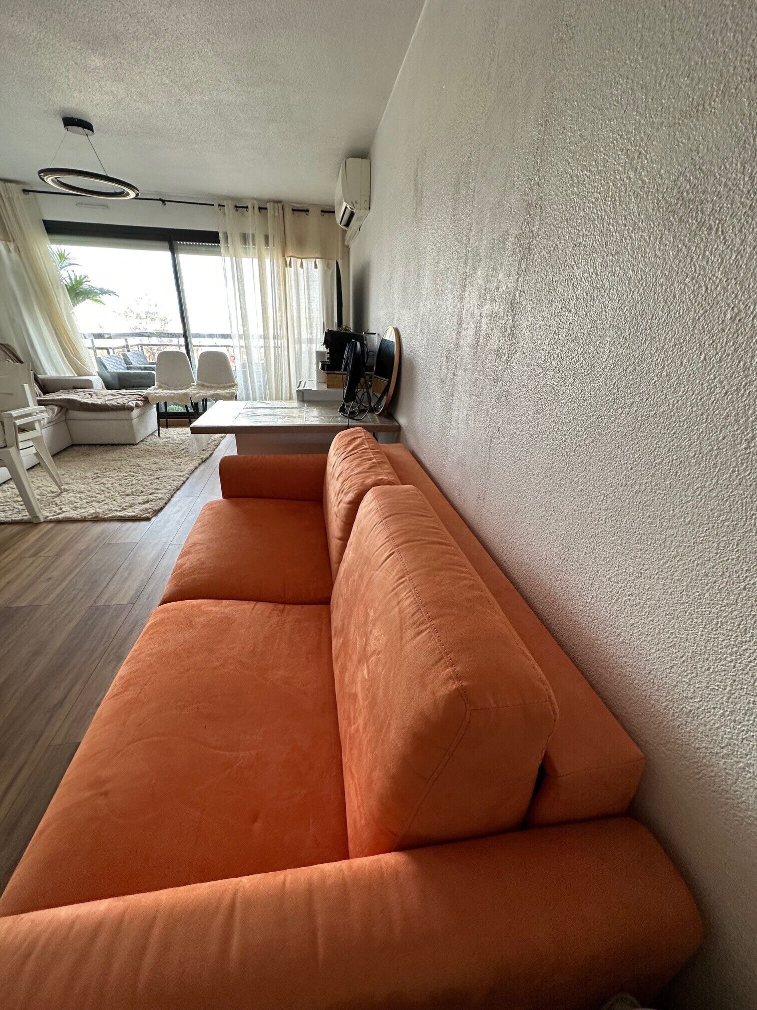 Una sala de estar moderna con un sofá grande color naranja, una mesa de comedor y vistas al exterior.