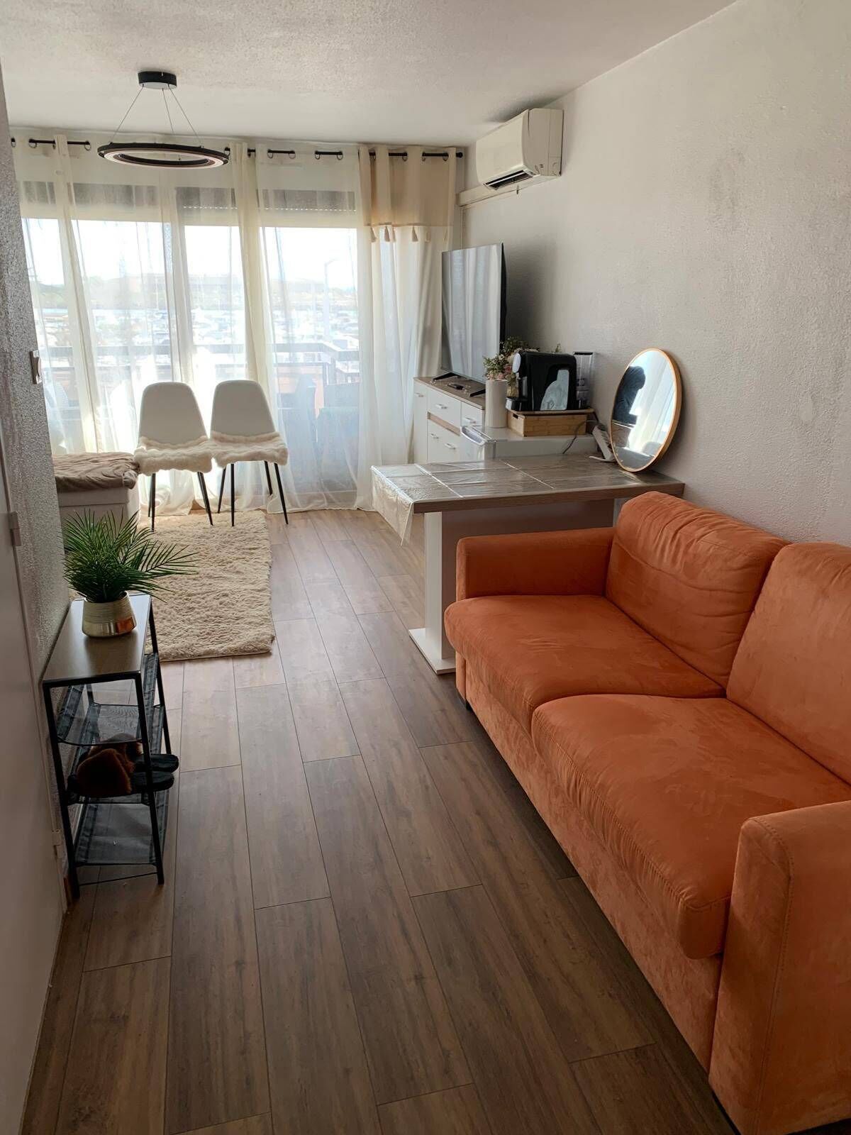 Un salon avec un canapé, un coin repas avec des chaises, une petite table, une plante en pot et un téléviseur.