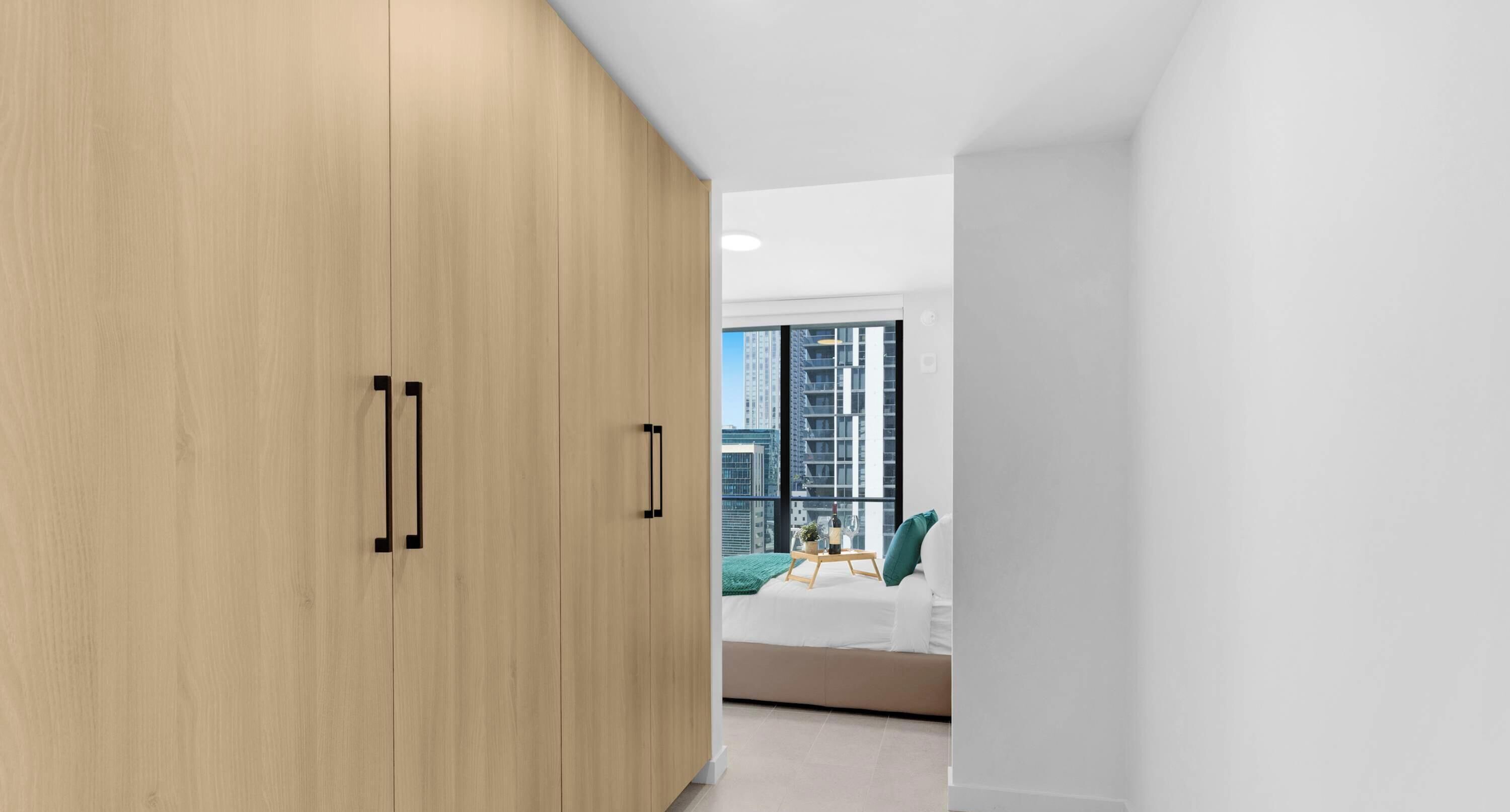 Una camera da letto moderna con un ampio armadio, un letto con una coperta verde e vista sulla città attraverso una grande finestra.