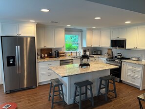 A modern kitchen with white cabinetry, stainless steel appliances, a granite countertop, and a central island with bar stools.