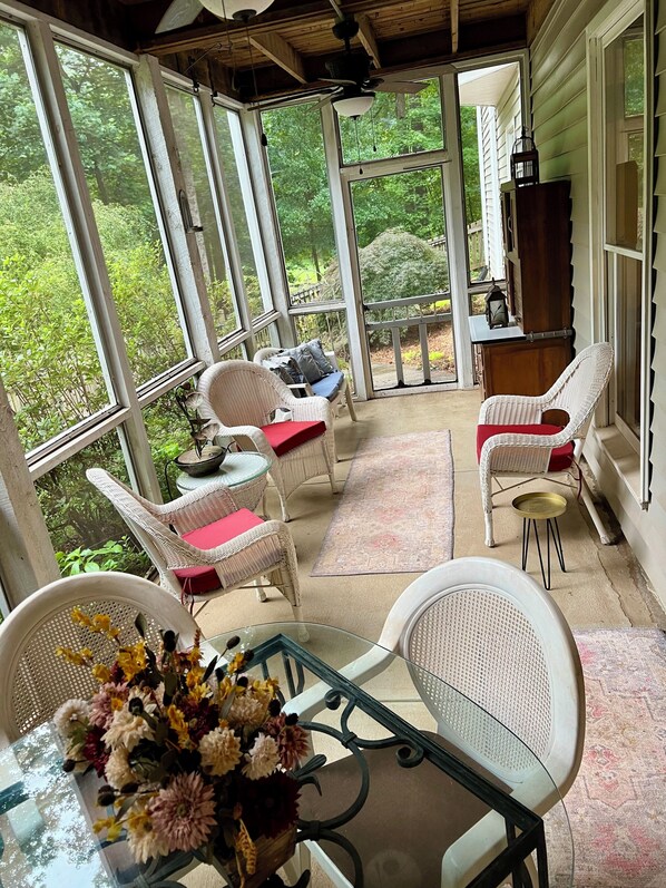 Un solárium con mobiliario de mimbre, una mesa de vidrio y vistas a la vegetación.