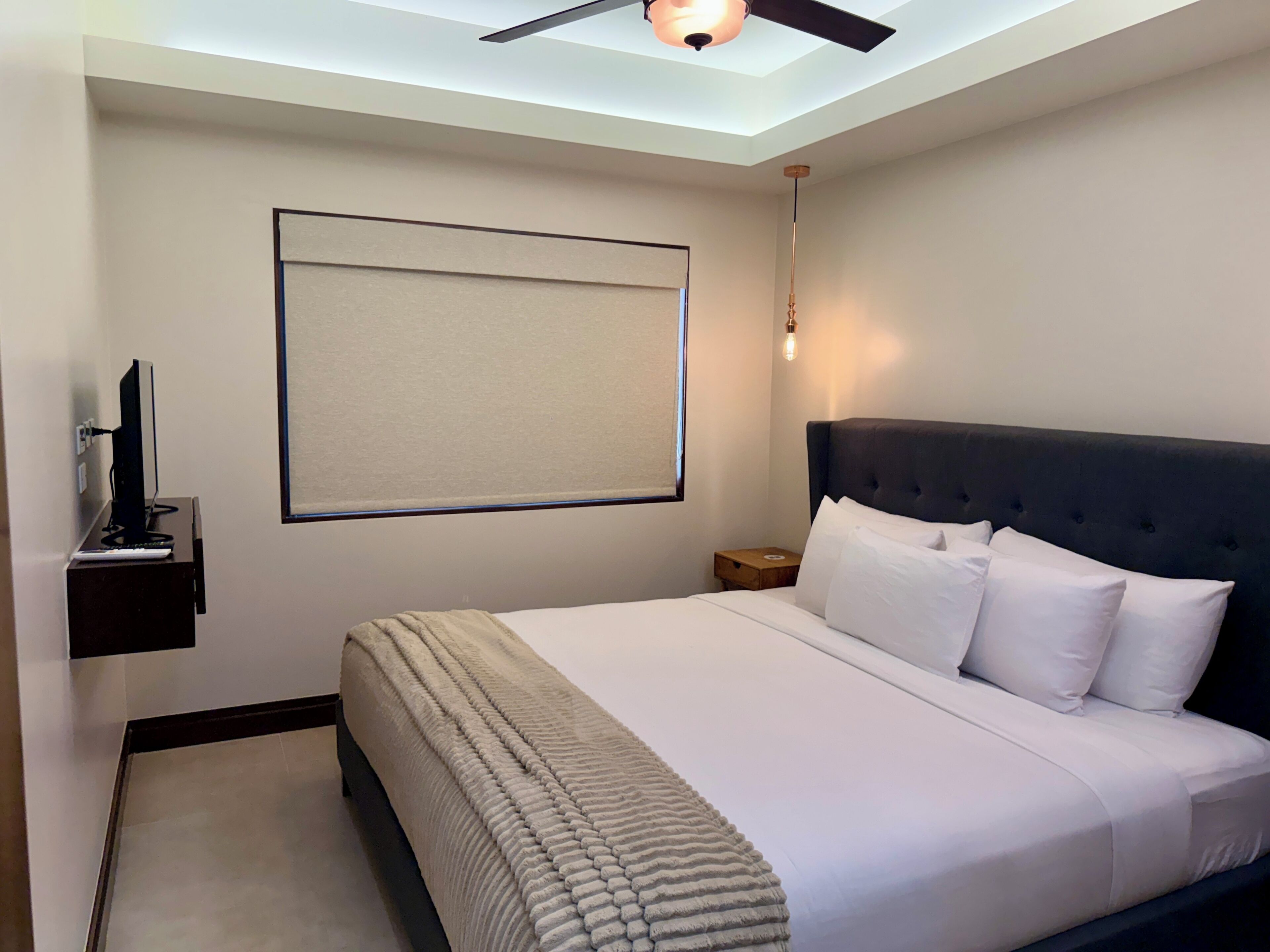 Ein Hotelzimmer mit einem Bett, einem Schreibtisch mit Computer, einem Deckenventilator und einer Wandleuchte.