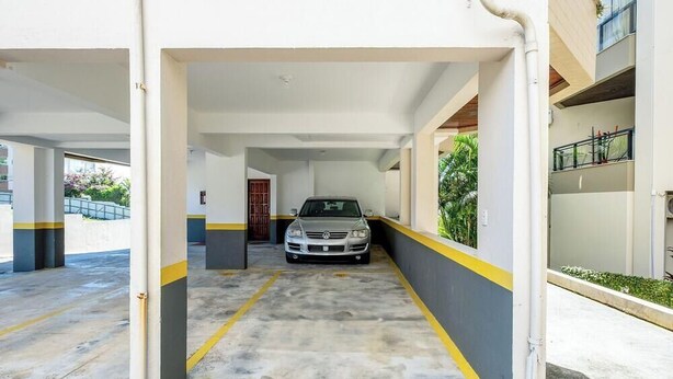 Uma garagem com um carro estacionado no centro, piso de concreto e paredes brancas com listras amarelas.