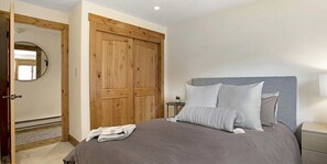 A bedroom with a bed, a wooden wardrobe, a round mirror, a bedside table, and a small potted plant. - Remodeled  East Vail Condo w/ Creekside Views, Free Shuttle Access!! (Vail)