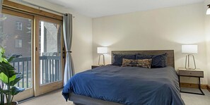 Een slaapkamer met een groot bed, twee nachtkastjes, een raam met gordijnen en uitzicht op een gebouw.
