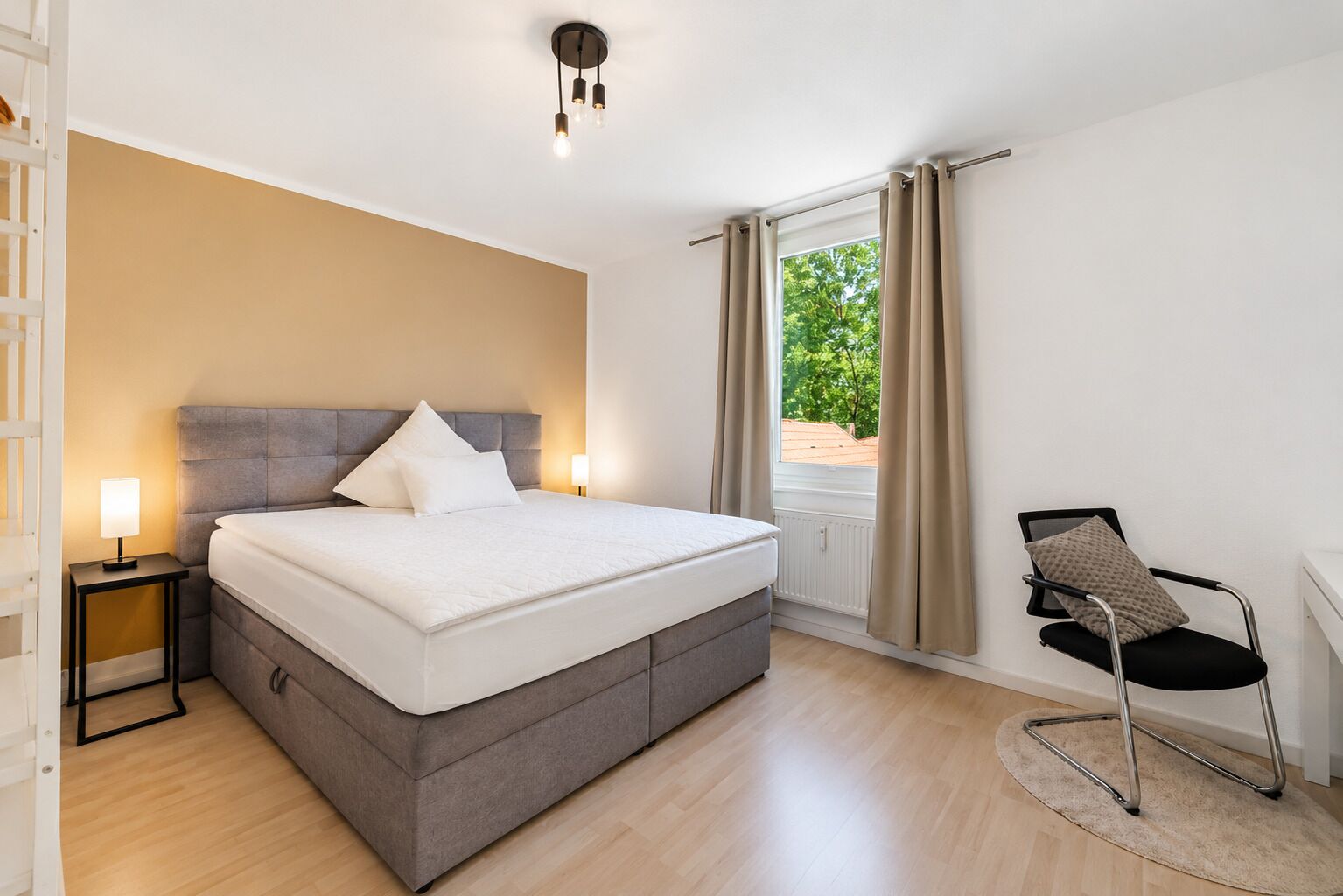 Ein modernes Schlafzimmer mit einem großen Bett, Nachttischlampen, einem Sessel und einem Fenster mit Vorhängen.