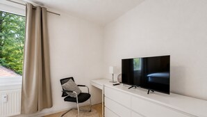 A modern room with a flat-screen TV, a desk, a chair, and a window with curtains. - Seibels Suites - Ruhrpott Oasis Altenessen (Essen)