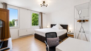 A modern hotel room with a bed, desk, chair, and a view of greenery outside. - Seibels Suites - Ruhrpott Oasis Altenessen (Essen)
