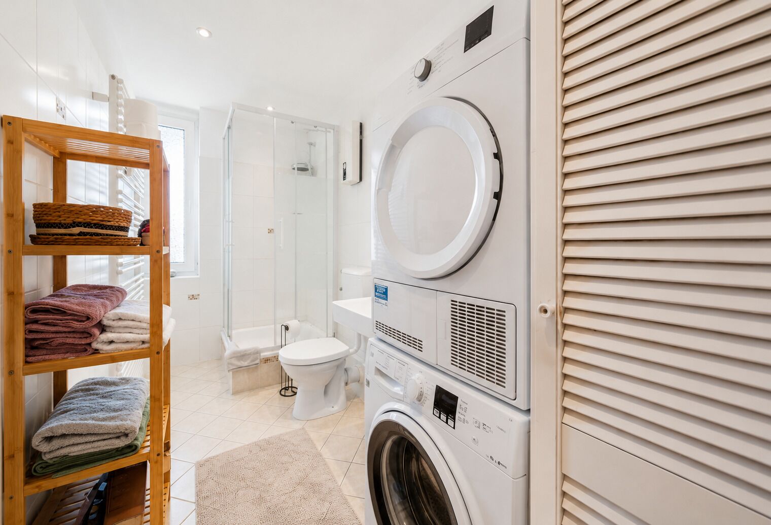 Une salle de bain moderne équipée d’un lave-linge, de toilettes et d’une douche à parois en verre.