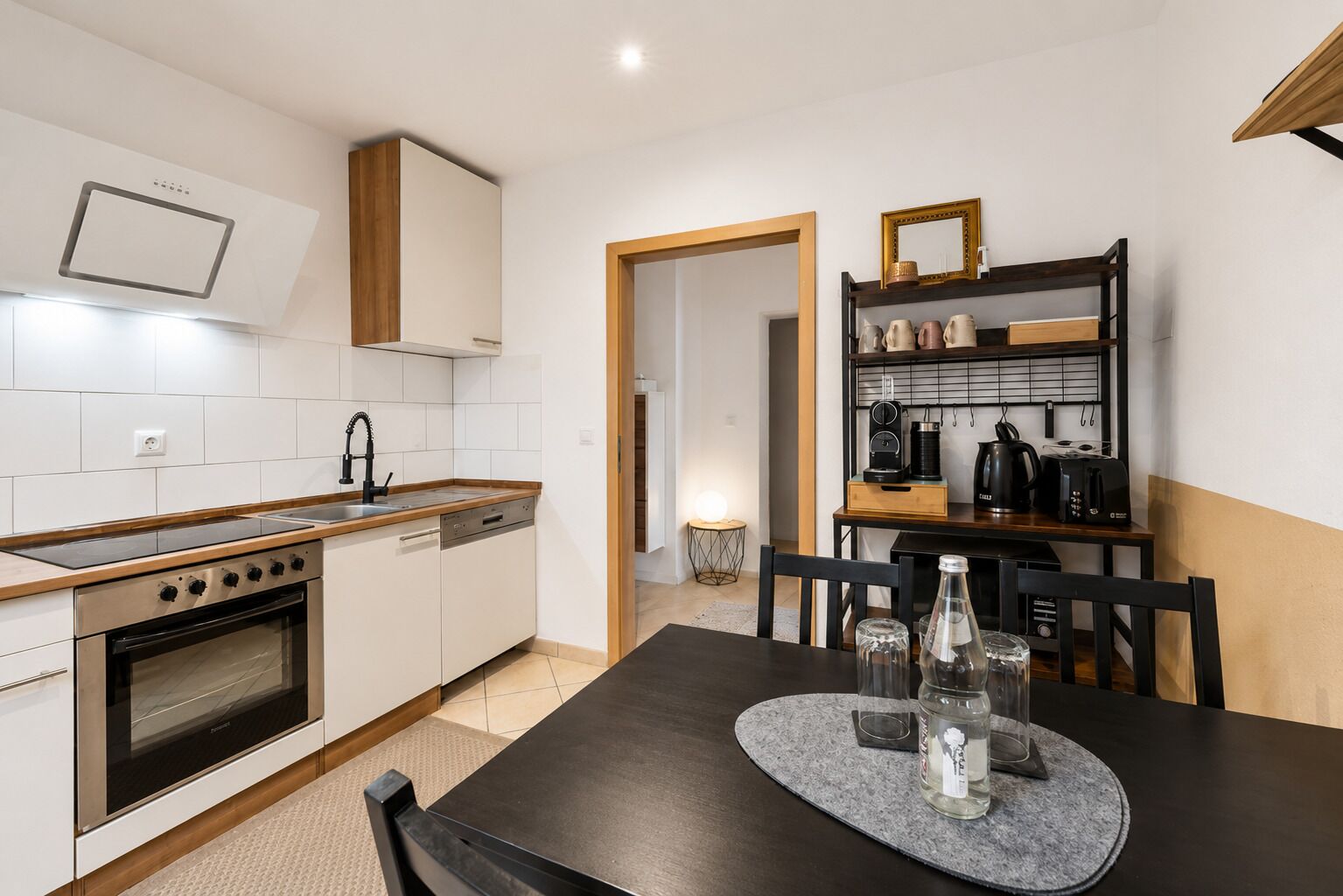 A modern kitchen with a stove, oven, and dishwasher, a dining table with chairs, and a coffee machine.