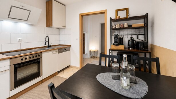 A modern kitchen with a stove, oven, and dishwasher, a dining table with chairs, and a coffee machine. - Seibels Suites - Ruhrpott Oasis Altenessen (Essen)
