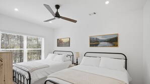 A bedroom with two beds, a ceiling fan, a window with blinds, and two landscape paintings on the wall. - Beautiful 5-bedroom lodge in Jasper Georgia (Big Canoe)