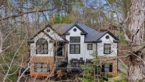 A two-story house with a stone foundation and white exterior walls, surrounded by trees. - Beautiful 5-bedroom lodge in Jasper Georgia (Big Canoe)