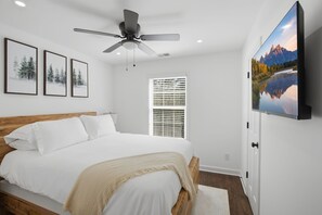 A bedroom with a bed, a ceiling fan, a window with blinds, and a TV mounted on the wall. - Beautiful 5-bedroom lodge in Jasper Georgia (Big Canoe)